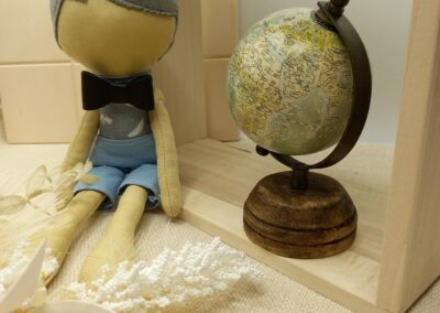 Poupée garçon en tissu, cheveux gris et short bleu pâle, près d'un globe
