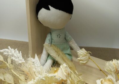 Poupée en tissu cheveux noirs et tenue vert d'eau parmi des fleurs séchées